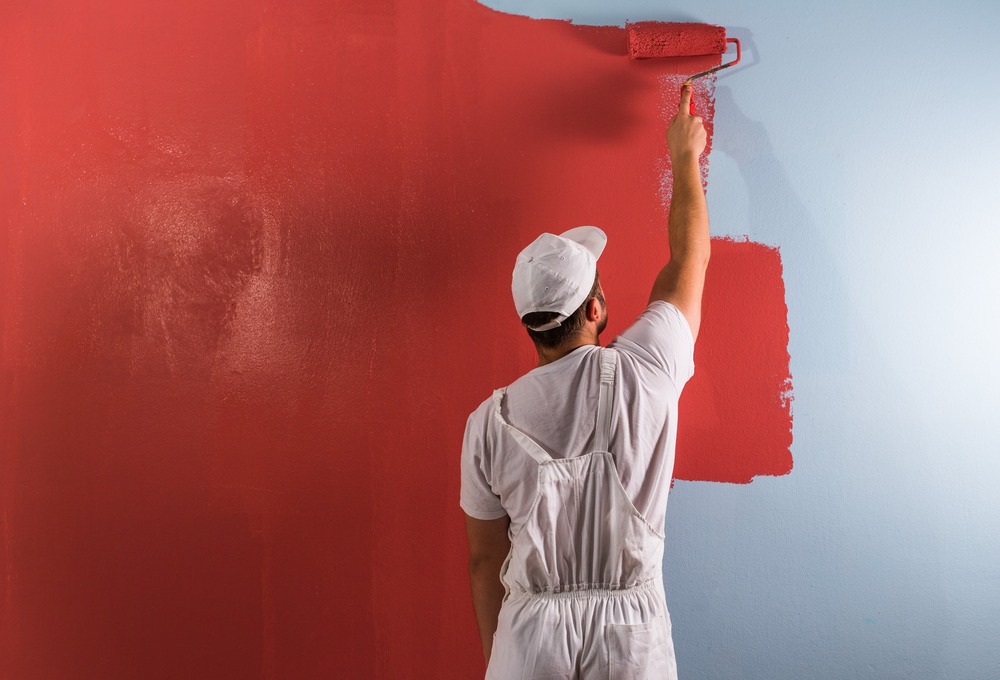 pintor aplicando color rojo con rodillo a pared
